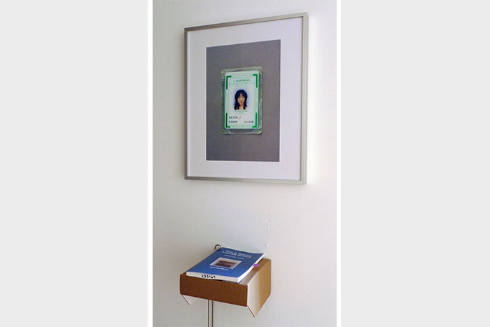 documentation photo of a framed photograph with a book on a cardboard shelf underneath the framed photo