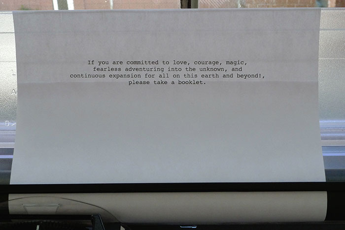 documentation photo of a note in a typewriter that reads, If you are committed to love, courage, magic,
        fearless adventuring into the unknown, and
        continuous expansion for all on this earth and beyond!,
        please take a booklet.